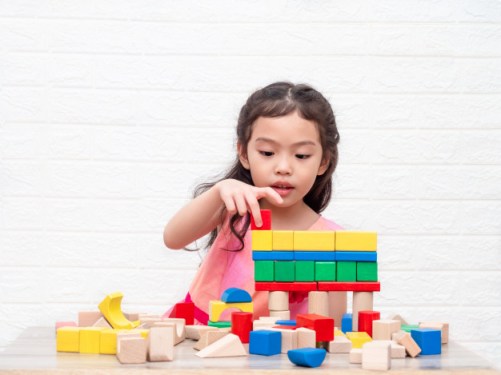little-cute-girl-playing-wooden-blocks-table-white-bricks-wall-background_112781-103